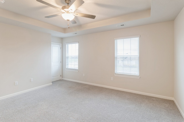 empty room featuring baseboards, visible vents, a tray ceiling, and light colored carpet