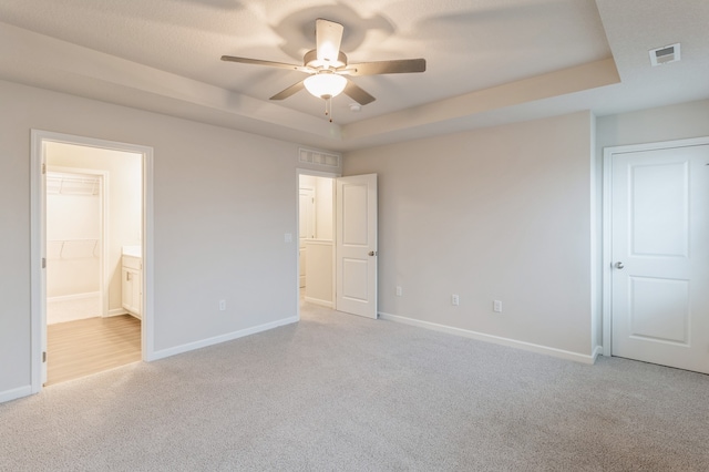 unfurnished bedroom featuring a spacious closet, light colored carpet, a raised ceiling, and ceiling fan