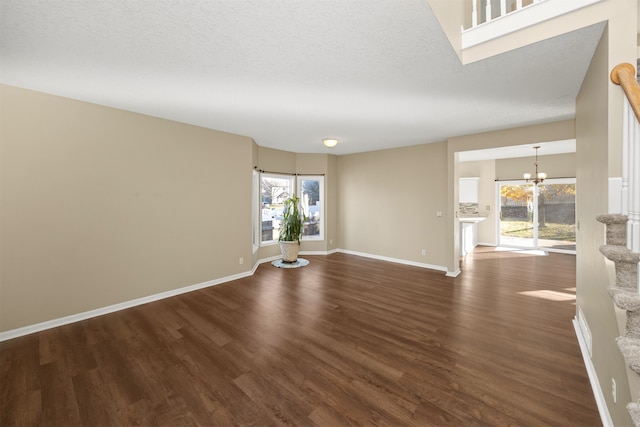 spare room featuring a chandelier, a textured ceiling, plenty of natural light, and dark wood-type flooring