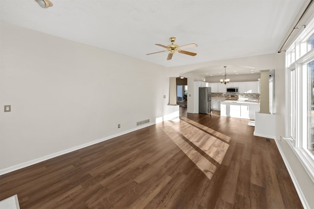 unfurnished living room with ceiling fan with notable chandelier and dark hardwood / wood-style flooring