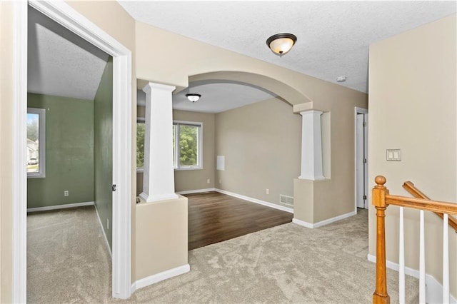 hall with decorative columns, carpet floors, and a textured ceiling