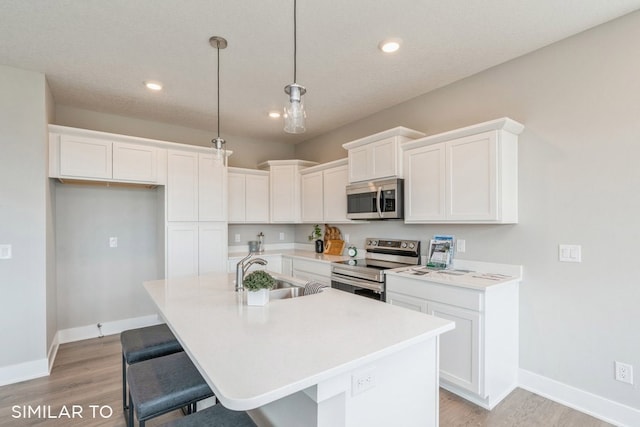 kitchen with appliances with stainless steel finishes, sink, pendant lighting, white cabinetry, and an island with sink