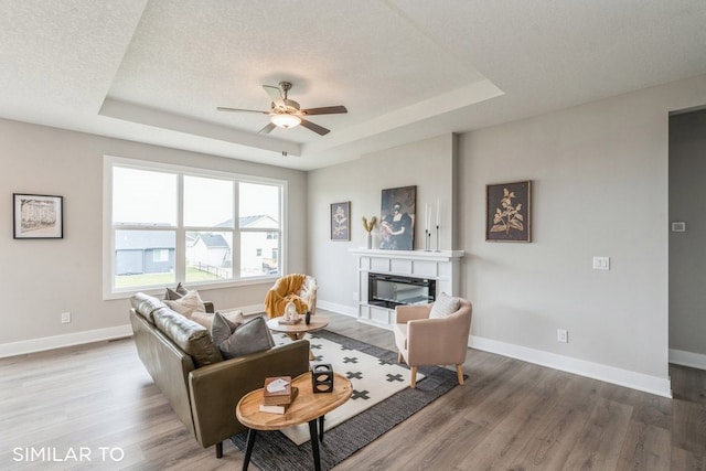 living room featuring hardwood / wood-style flooring, ceiling fan, a tray ceiling, and a textured ceiling