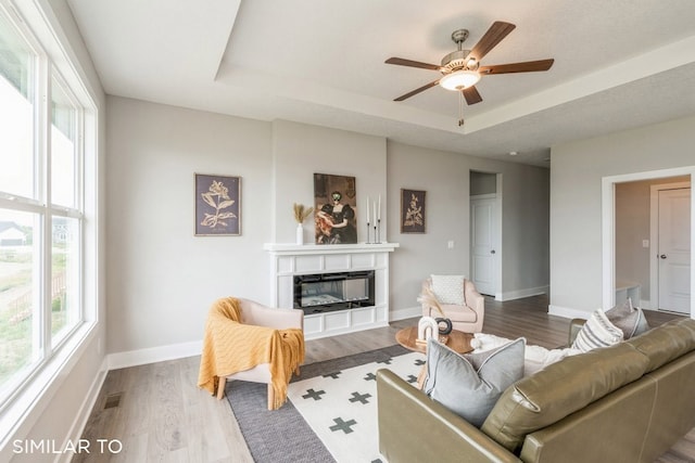 living room with ceiling fan, a tray ceiling, and light hardwood / wood-style floors