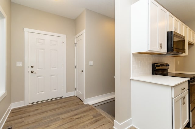 kitchen with range with electric stovetop, light wood-type flooring, white cabinetry, and backsplash