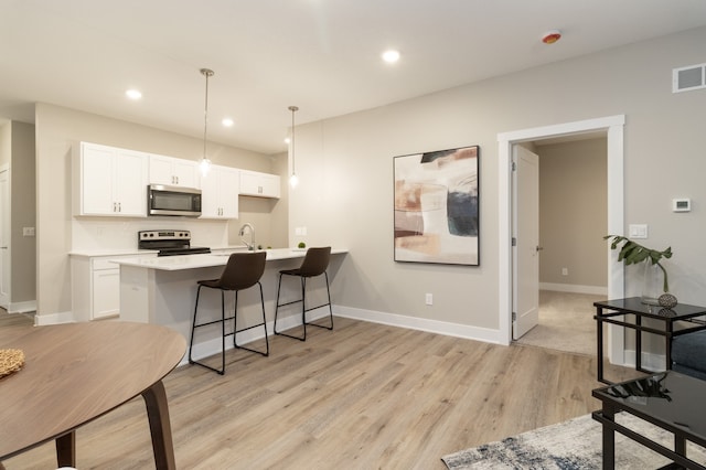 kitchen with white cabinets, pendant lighting, light wood-type flooring, and appliances with stainless steel finishes