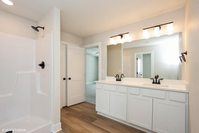 full bathroom featuring double vanity, wood finished floors, walk in shower, and a sink