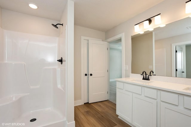 bathroom with double vanity, walk in shower, a sink, and wood finished floors