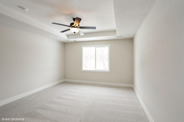 spare room with a textured ceiling, light colored carpet, visible vents, baseboards, and a raised ceiling