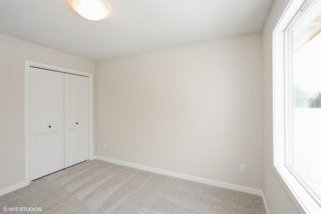 unfurnished bedroom featuring light carpet, baseboards, and a closet