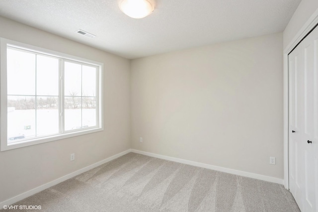 unfurnished bedroom with a textured ceiling, visible vents, baseboards, a closet, and carpet