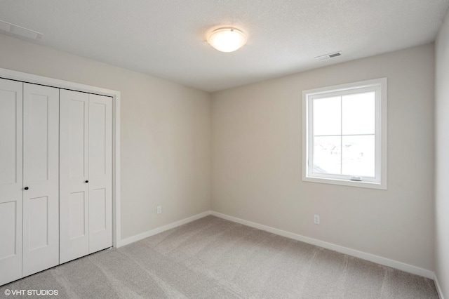 unfurnished bedroom with baseboards, visible vents, light colored carpet, a textured ceiling, and a closet