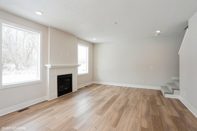 unfurnished living room with visible vents, a fireplace, light wood-style flooring, and stairs