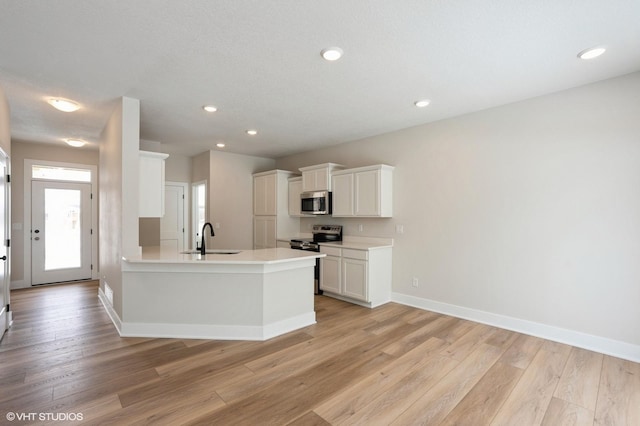 kitchen featuring light wood finished floors, light countertops, appliances with stainless steel finishes, white cabinetry, and a sink