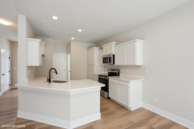 kitchen featuring appliances with stainless steel finishes, light countertops, light wood-style floors, white cabinetry, and a sink