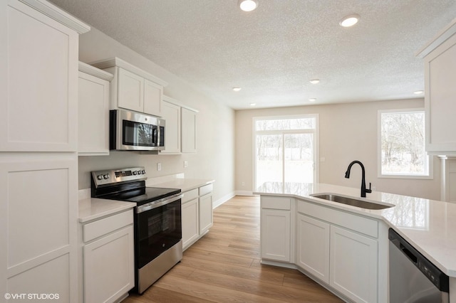 kitchen featuring stainless steel appliances, a sink, white cabinetry, light wood-style floors, and light countertops