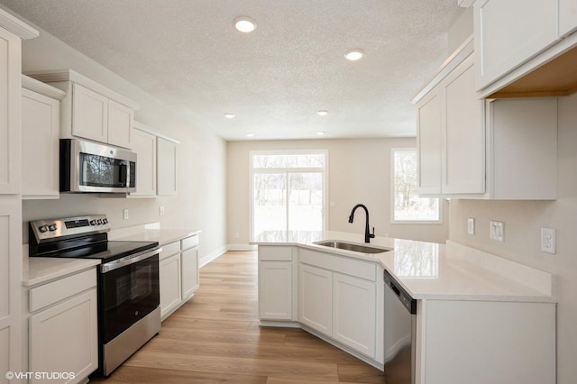 kitchen featuring stainless steel appliances, light countertops, light wood-style flooring, white cabinetry, and a sink