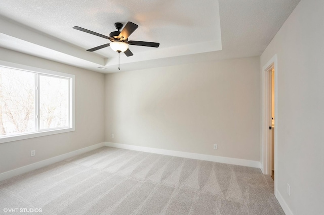 unfurnished room with a tray ceiling, light carpet, ceiling fan, a textured ceiling, and baseboards