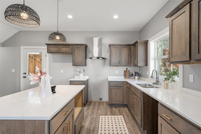 kitchen featuring sink, wall chimney range hood, decorative light fixtures, hardwood / wood-style flooring, and a center island