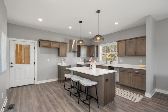 kitchen with wall chimney exhaust hood, hanging light fixtures, hardwood / wood-style flooring, and a kitchen island