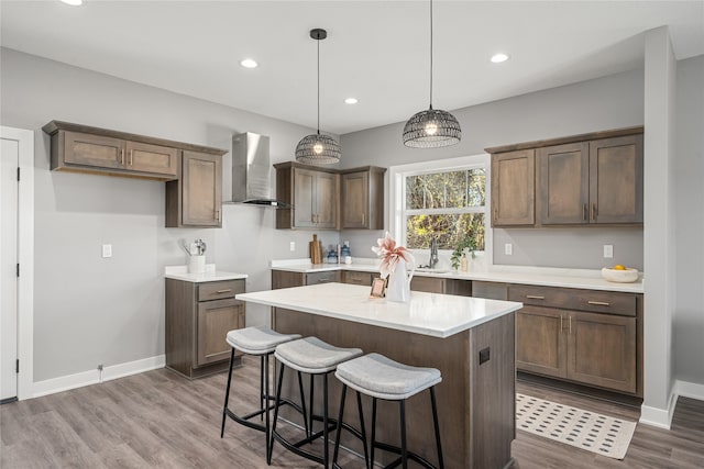 kitchen with decorative light fixtures, wall chimney range hood, dark wood-type flooring, and a kitchen island