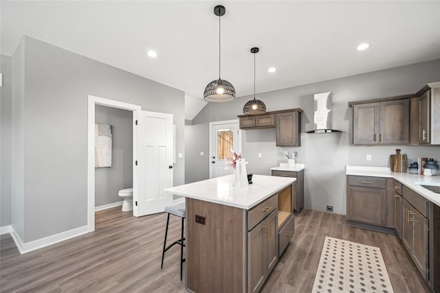 kitchen featuring wall chimney exhaust hood, dark wood-type flooring, pendant lighting, a breakfast bar, and a kitchen island