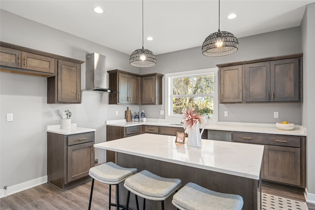 kitchen with light stone countertops, pendant lighting, a kitchen island, and wall chimney range hood