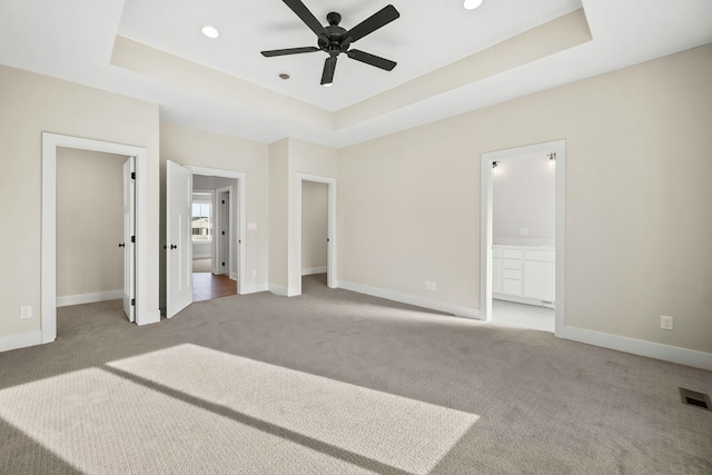 unfurnished bedroom with a tray ceiling, light colored carpet, ceiling fan, and ensuite bathroom