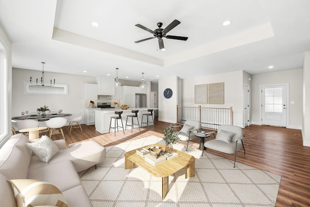 living room featuring a raised ceiling, ceiling fan with notable chandelier, and light wood-type flooring