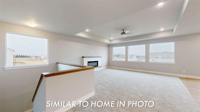 unfurnished living room with a raised ceiling, light colored carpet, and ceiling fan