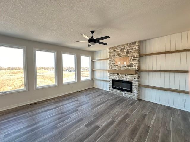 unfurnished living room featuring ceiling fan, plenty of natural light, a stone fireplace, and dark wood-type flooring