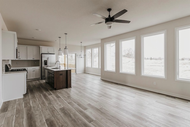 kitchen with sink, light hardwood / wood-style flooring, a kitchen island with sink, stainless steel appliances, and decorative light fixtures