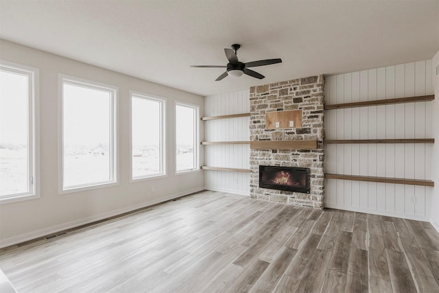 unfurnished living room featuring ceiling fan, a stone fireplace, and light wood-type flooring