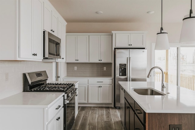 kitchen with sink, appliances with stainless steel finishes, pendant lighting, a kitchen island with sink, and white cabinets