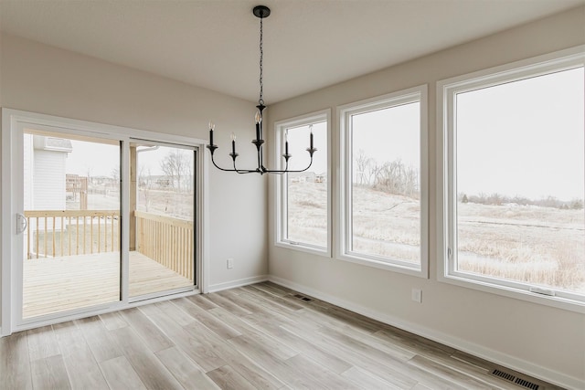 unfurnished dining area with a chandelier and light hardwood / wood-style flooring