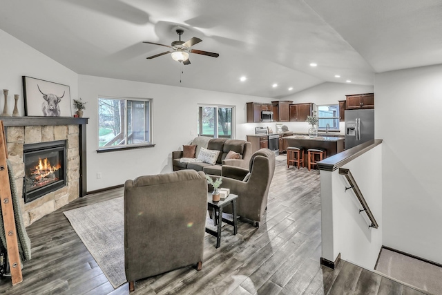 living area with plenty of natural light, vaulted ceiling, a tiled fireplace, and wood finished floors