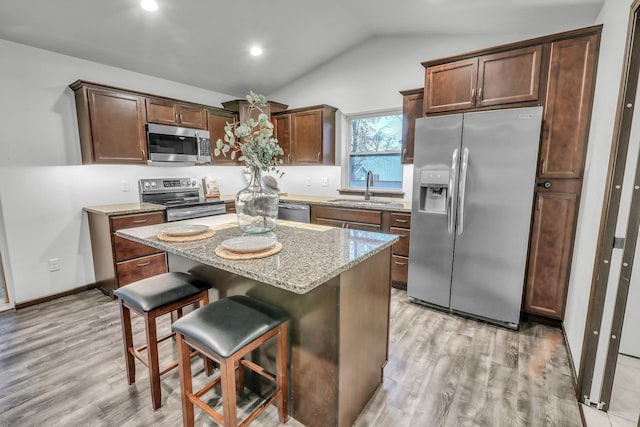 kitchen with lofted ceiling, light wood-style floors, stainless steel appliances, and a sink