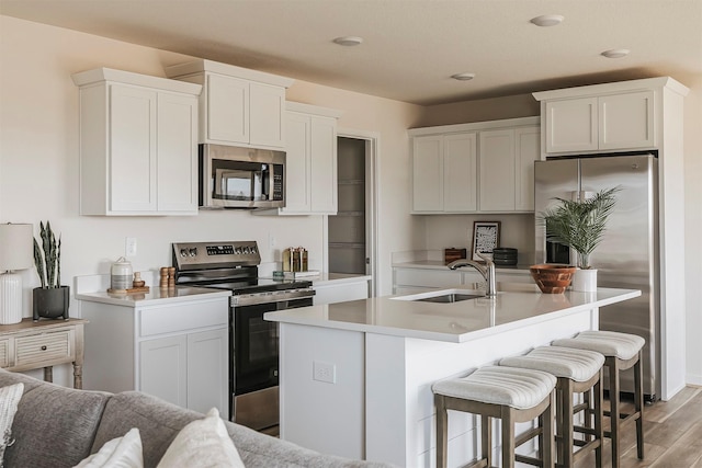 kitchen with appliances with stainless steel finishes, sink, white cabinets, light hardwood / wood-style floors, and a center island with sink