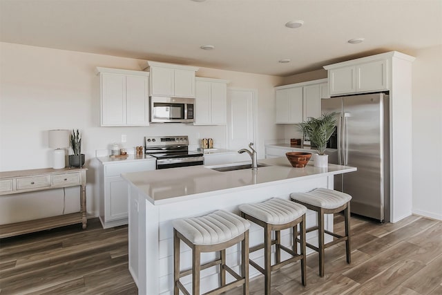 kitchen with sink, appliances with stainless steel finishes, dark hardwood / wood-style floors, a kitchen island with sink, and white cabinets