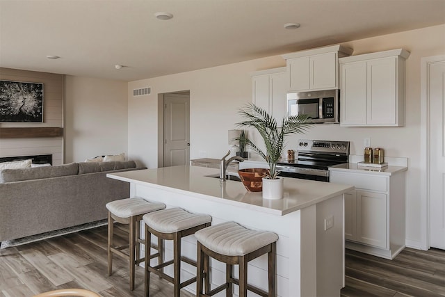 kitchen with dark hardwood / wood-style flooring, a center island with sink, white cabinets, and appliances with stainless steel finishes