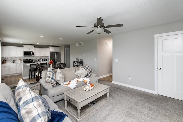 living room with a textured ceiling, light colored carpet, and ceiling fan