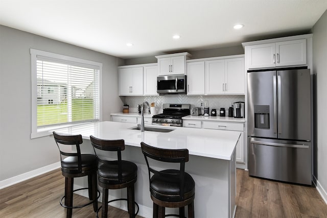 kitchen featuring dark wood-type flooring, a center island with sink, sink, appliances with stainless steel finishes, and white cabinetry