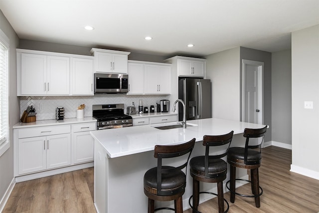 kitchen with a kitchen island with sink, sink, white cabinets, and appliances with stainless steel finishes