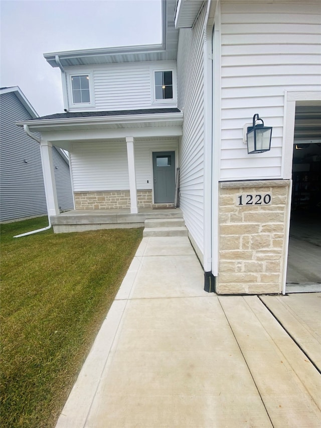 view of exterior entry with a lawn and a porch