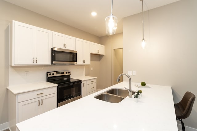 kitchen featuring white cabinetry, sink, stainless steel appliances, pendant lighting, and a kitchen bar