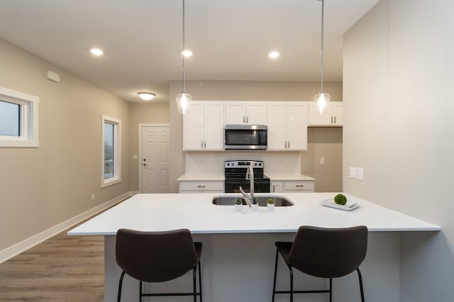 kitchen featuring pendant lighting, stainless steel appliances, white cabinetry, and a kitchen island with sink