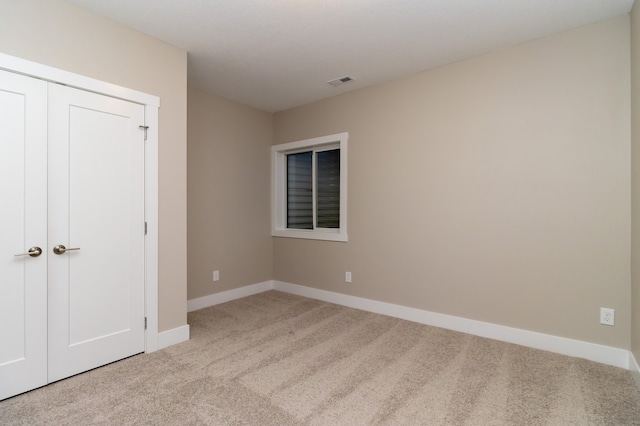 unfurnished bedroom with light colored carpet and a closet