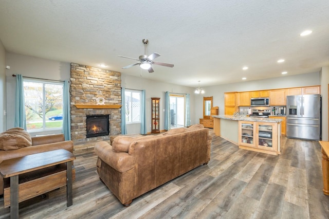 living room featuring dark hardwood / wood-style flooring, a stone fireplace, a textured ceiling, and ceiling fan with notable chandelier