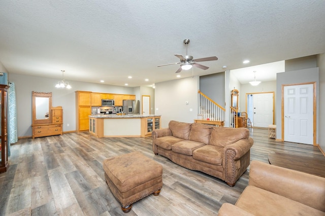 living room featuring ceiling fan with notable chandelier, a textured ceiling, and light wood-type flooring