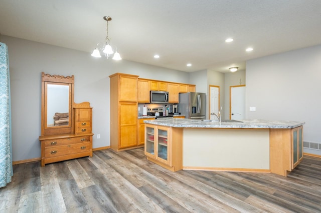 kitchen with stainless steel appliances, pendant lighting, a center island with sink, a chandelier, and hardwood / wood-style floors